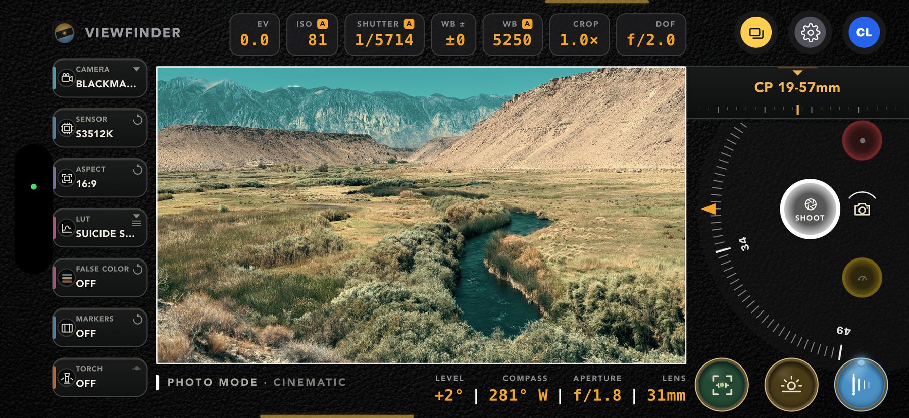 CamPlot Director's Viewfinder in Photo mode — a wide valley with a creek running through it, framed through a Blackmagic body on its S35 12K window, with EV, ISO, shutter, white balance and a depth-of-field readout across the top and the lens roll on the right